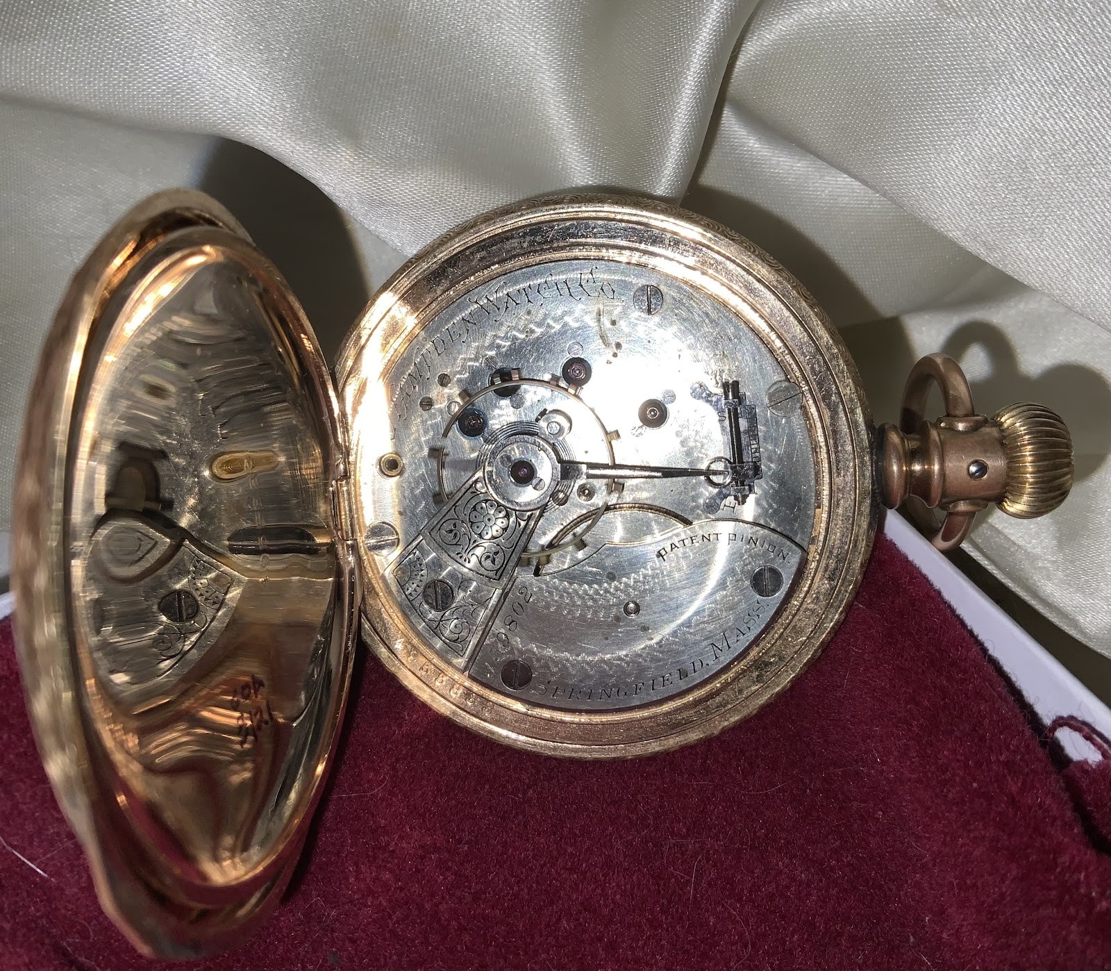 An open gold pocket watch showing its movement, resting on velvet